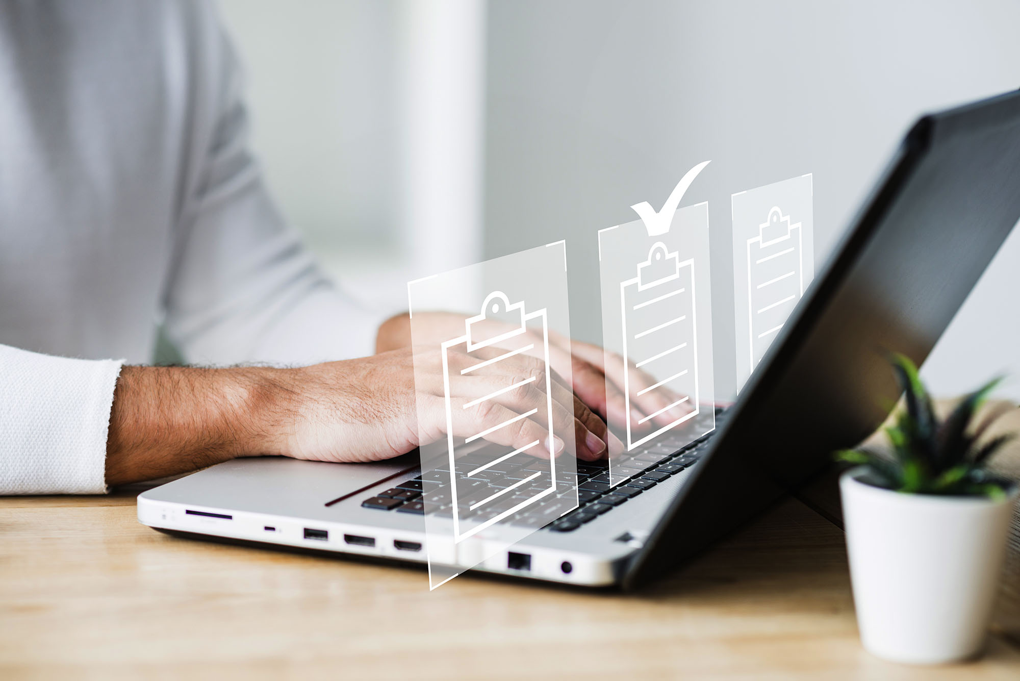 Человек в светлой рубашке работает на ноутбуке. На экране ноутбука видны иконки документов.